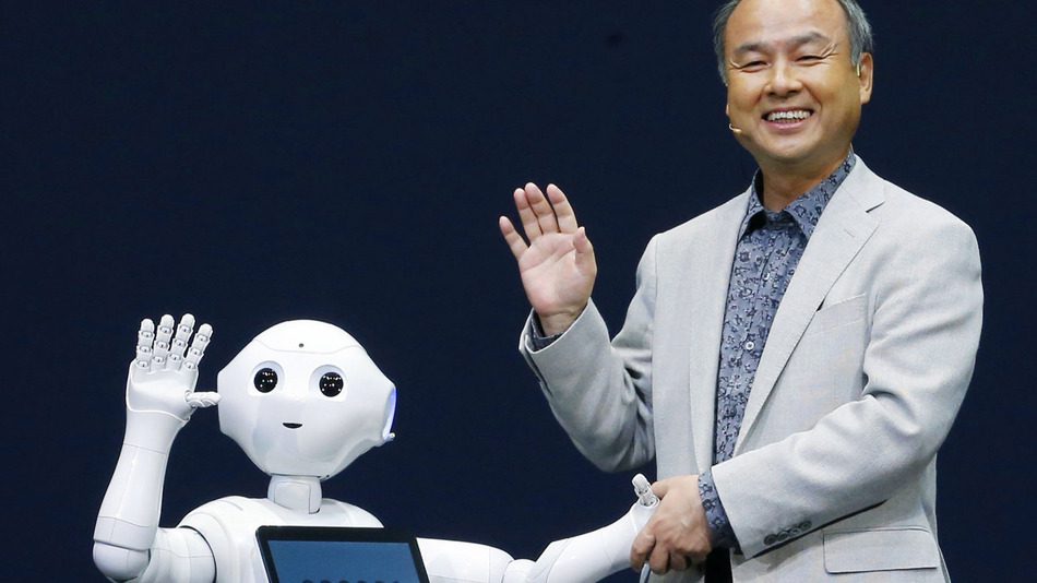 A photo of a person and a robot interacting. The person is wearing a gray suit and is waving. The robot is white and has a screen on its chest. The robot is also waving. The background is a blue wall with a white stripe.